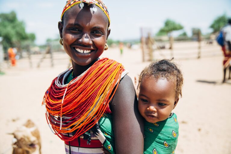 kenyan woman in bright red and yellow neckpiece with baby on her back