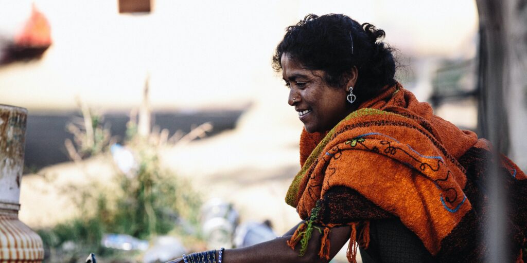 A woman in India wearing jewelry and a scarf smiles at her work station